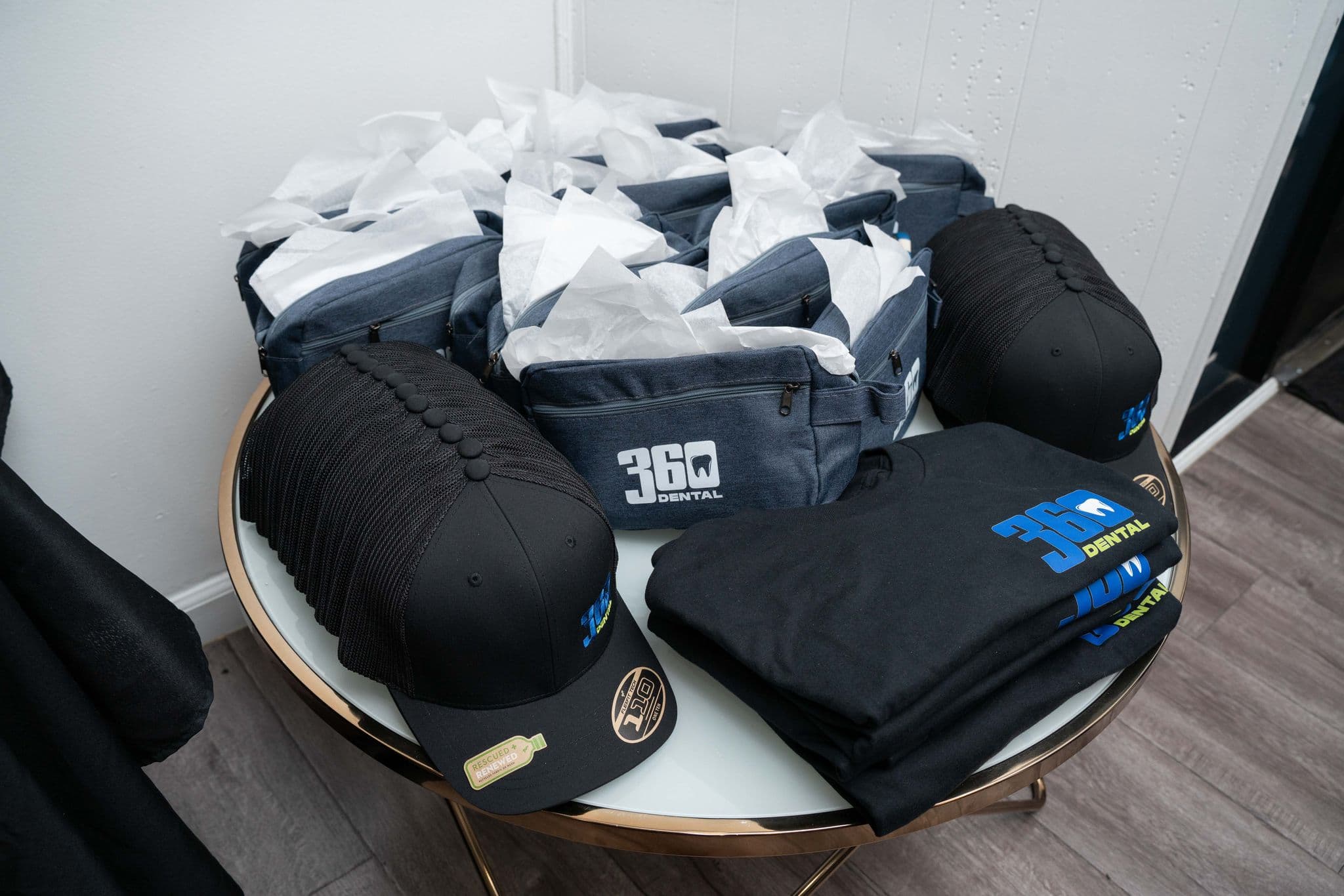 Branded 360 Dental caps, shirts and bags laid out as anniversary gifts