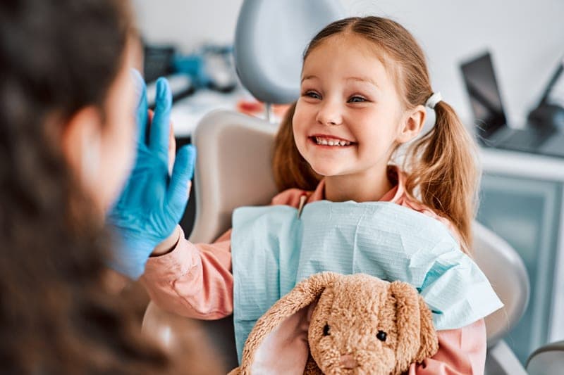 A young child in the dental chair, holding a soft toy