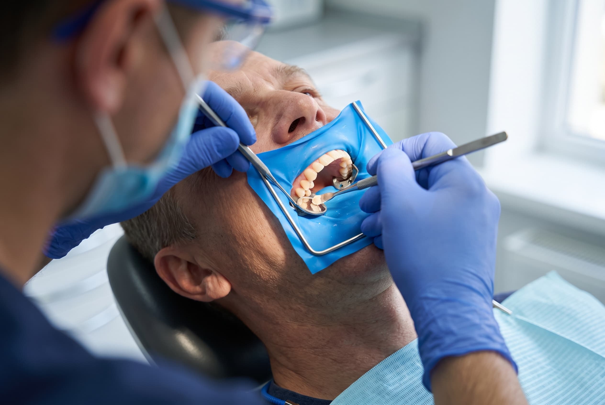 A tooth isolated behind a rubber dam while the dentist works with a mirror and instrument