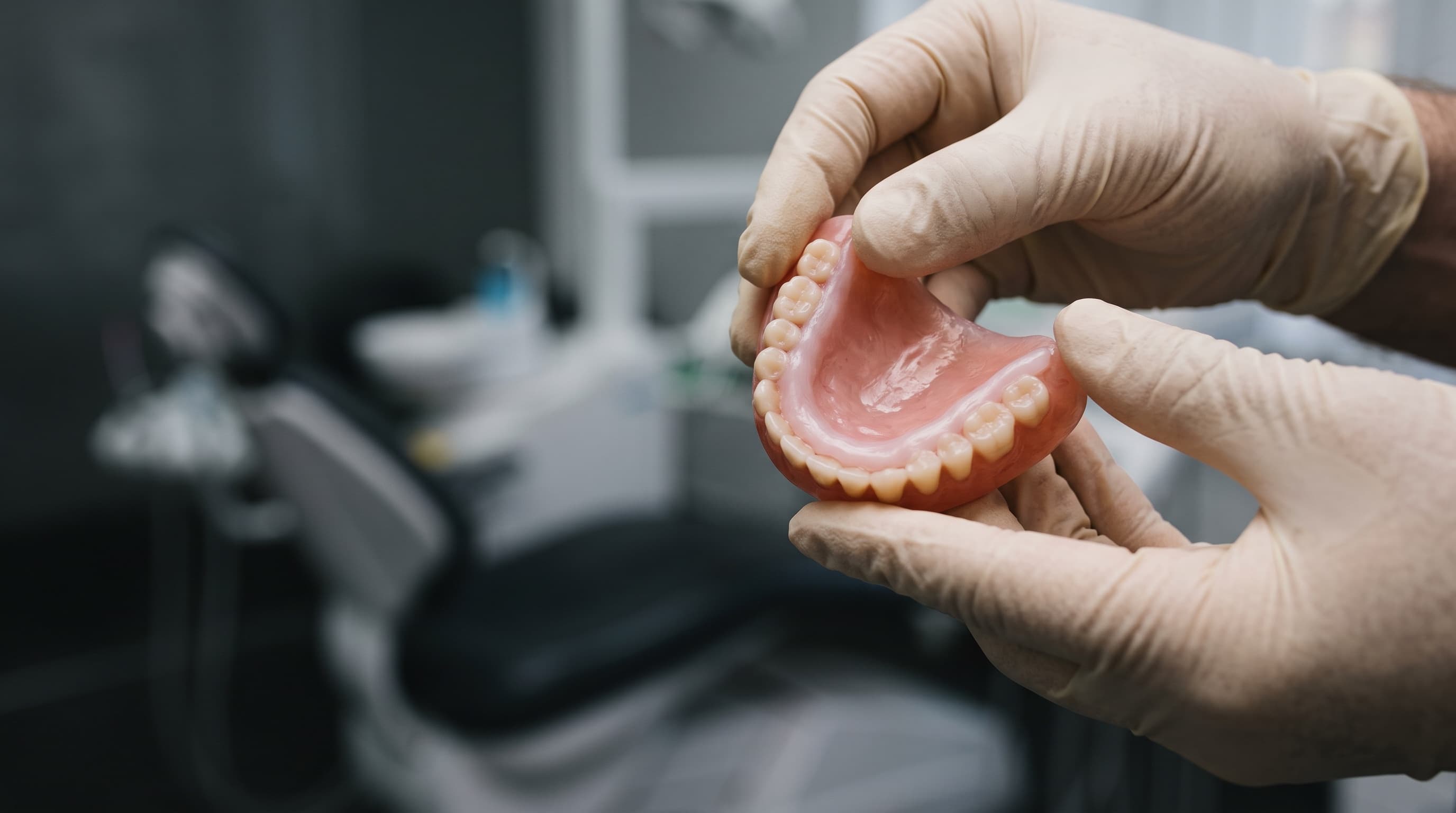 Gloved hands turning a denture to show the soft liner on its fitting surface