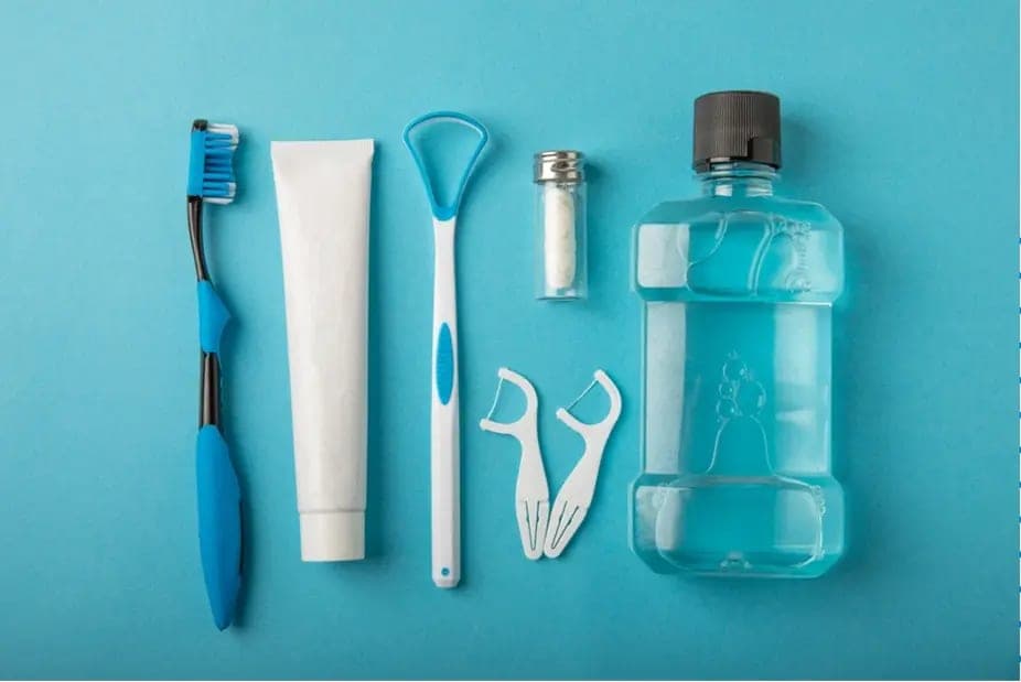 A toothbrush, paste, floss, scraper and mouthwash laid out in a row