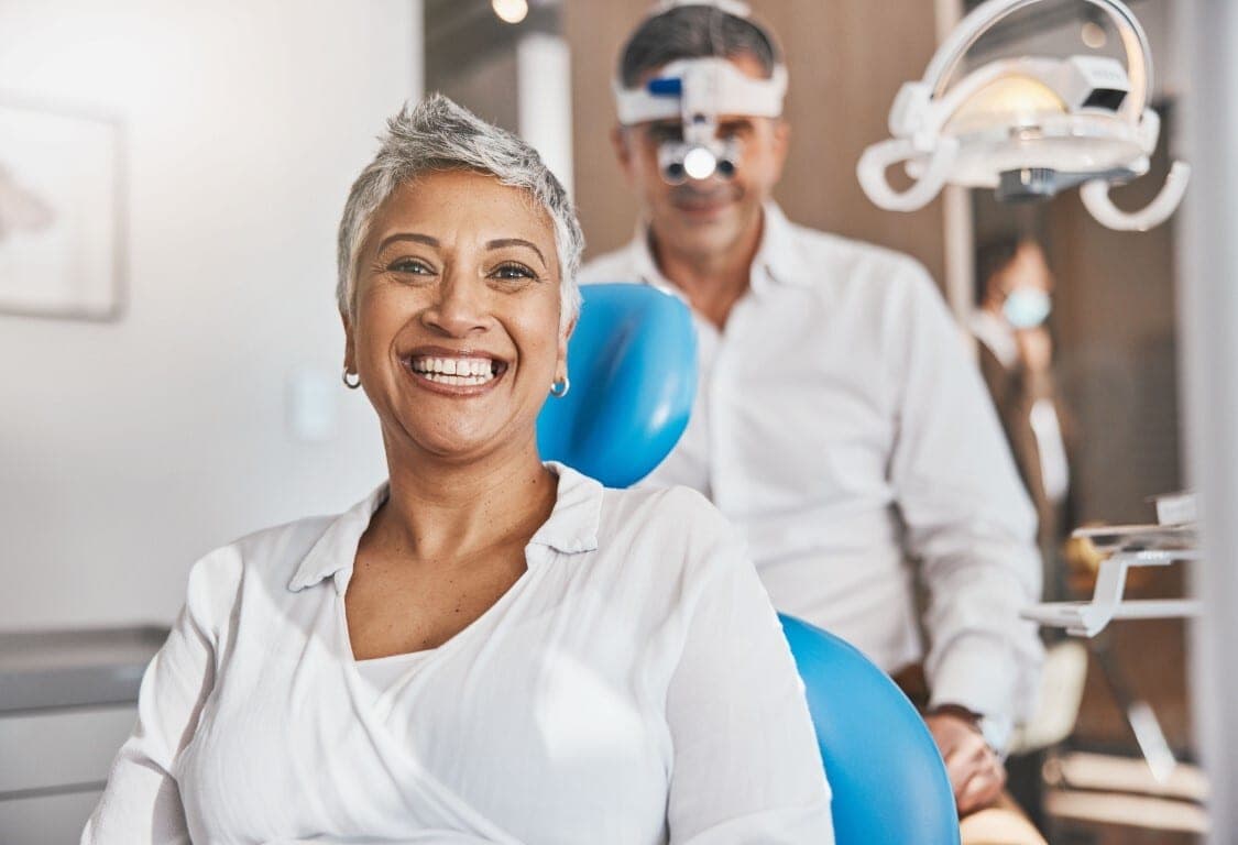 An older patient smiling in the chair beside her dentist