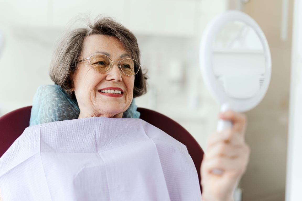 An older patient checking her smile in a hand mirror at a review appointment