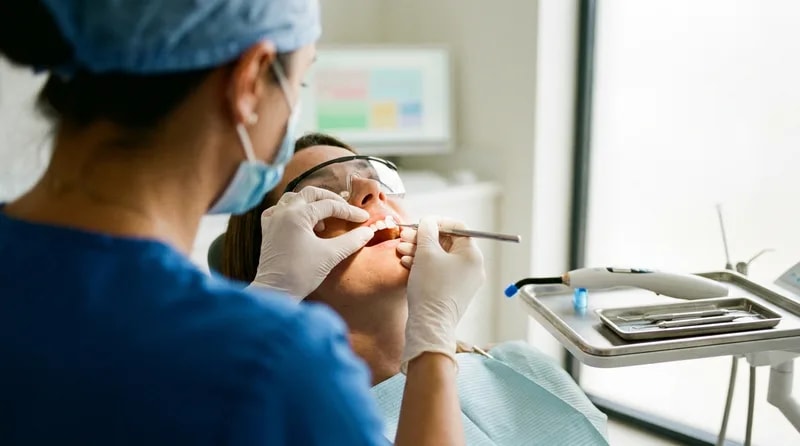 Dentist bonding a porcelain veneer onto a patient's front tooth in a treatment room