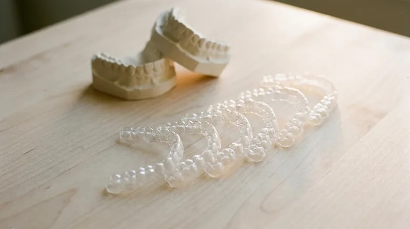 Sequence of clear aligner trays fanned out in order beside plaster study models